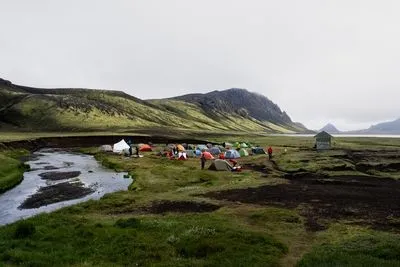 Kleurrijke tenten op een camping in de hooglanden naast een rivier, met een kleine hut en groene bergen