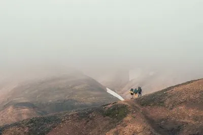 Two hikers with backpacks on a ridge, almost swallowed by thick fog