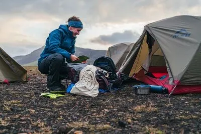 A hiker in a blue jacket sorting gear next to her tent at a highland campsite